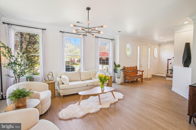 living room featuring an inviting chandelier, visible vents, light wood-type flooring, and ornamental molding