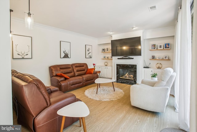 living area with ornamental molding, a high end fireplace, visible vents, and wood finished floors