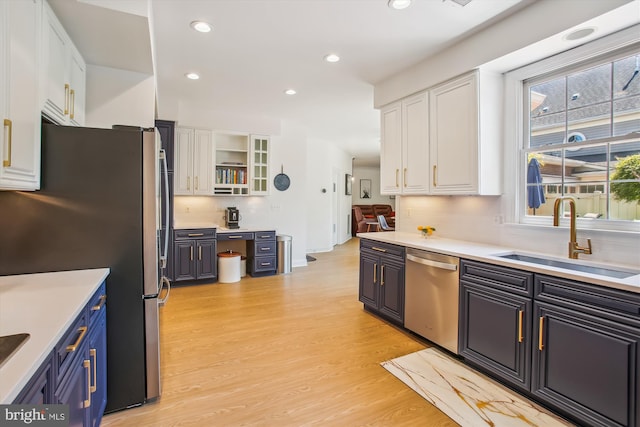 kitchen with tasteful backsplash, stainless steel appliances, light wood finished floors, a sink, and white cabinetry