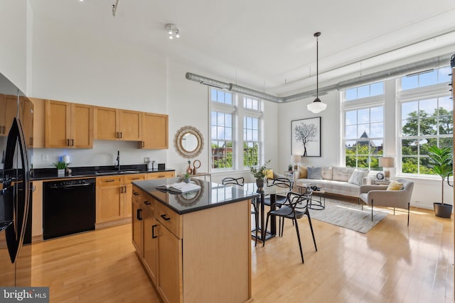 kitchen featuring black appliances, dark countertops, a towering ceiling, light wood-type flooring, and a sink