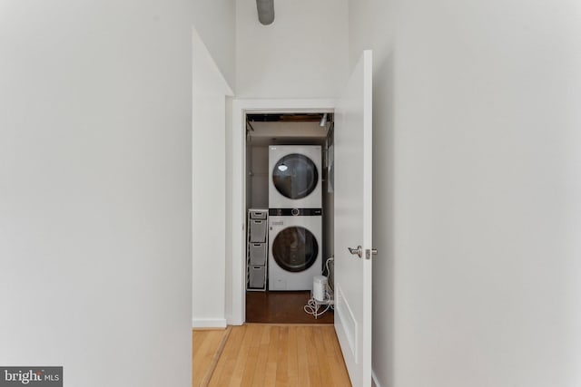 laundry room with stacked washing machine and dryer, light wood-type flooring, and baseboards