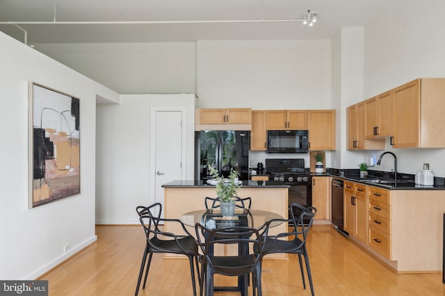 kitchen with black appliances, a sink, a towering ceiling, dark countertops, and a center island