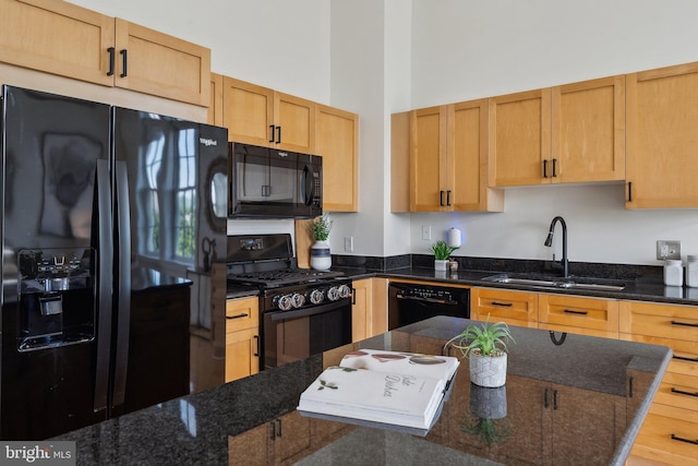 kitchen with black appliances, a sink, dark stone counters, and a towering ceiling