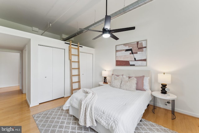 bedroom featuring a barn door, wood finished floors, multiple closets, baseboards, and ceiling fan