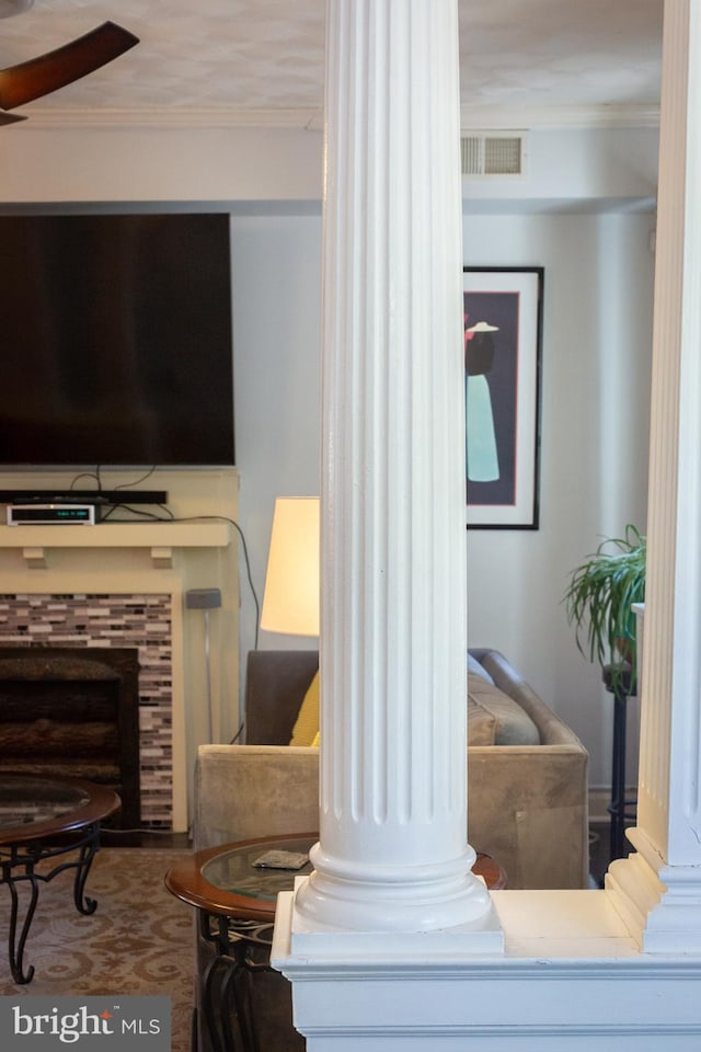living area featuring ceiling fan, decorative columns, visible vents, crown molding, and a tiled fireplace