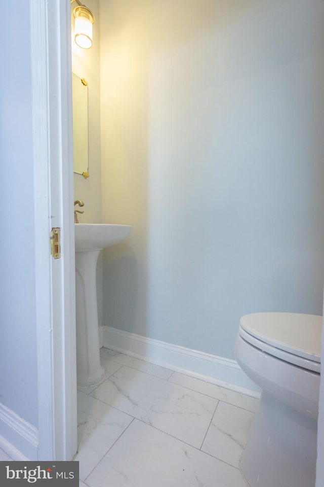 half bath with toilet, baseboards, and marble finish floor