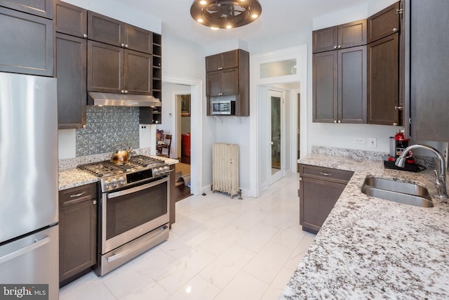kitchen featuring dark brown cabinets, a sink, under cabinet range hood, radiator, and stainless steel appliances