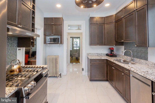 kitchen featuring marble finish floor, radiator heating unit, under cabinet range hood, a sink, and appliances with stainless steel finishes