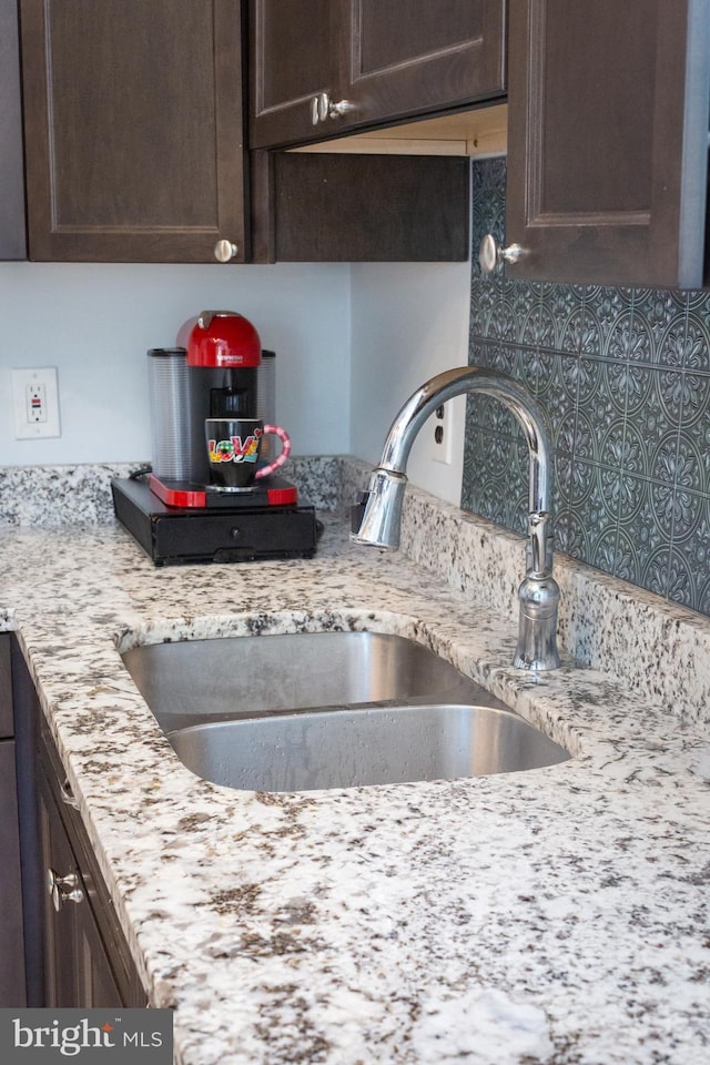 kitchen featuring dark brown cabinets, light stone countertops, a sink, and tasteful backsplash