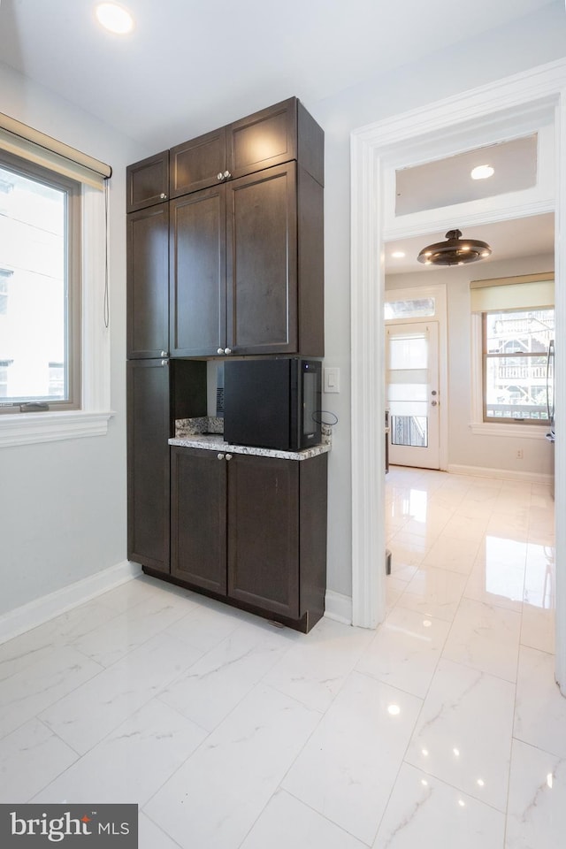 kitchen featuring baseboards, dark brown cabinetry, and marble finish floor