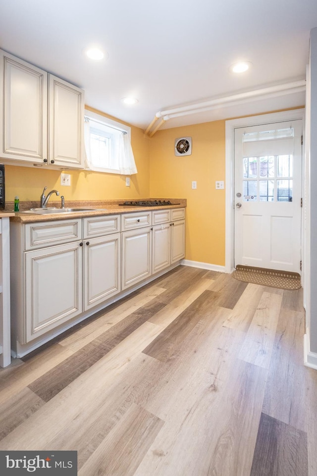 kitchen with a sink, light wood finished floors, light countertops, recessed lighting, and baseboards