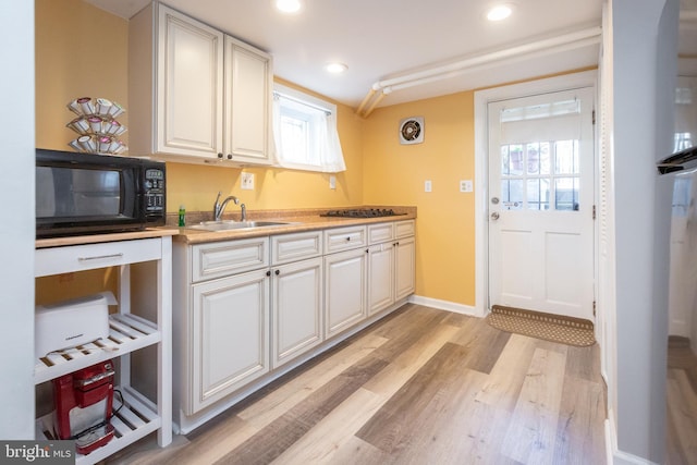 kitchen featuring black microwave, a sink, light countertops, light wood-style flooring, and baseboards