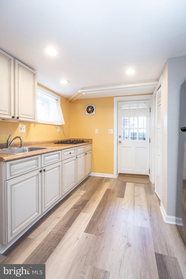 kitchen featuring light wood-type flooring, a sink, baseboards, and a wealth of natural light