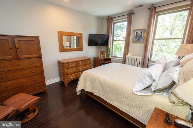 bedroom featuring visible vents, baseboards, dark wood-style flooring, and radiator heating unit
