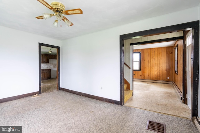 spare room with a ceiling fan, wooden walls, baseboards, carpet flooring, and visible vents