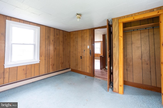 unfurnished bedroom with a baseboard heating unit, baseboard heating, carpet flooring, and wooden walls