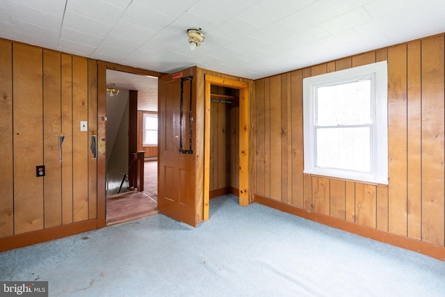 unfurnished bedroom with a baseboard radiator, wood walls, carpet flooring, and a closet