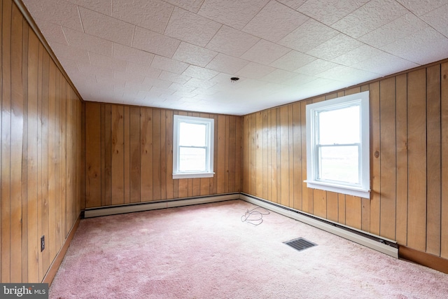 carpeted spare room featuring visible vents, wood walls, and a baseboard heating unit