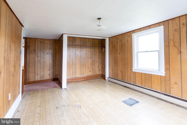unfurnished bedroom with a baseboard heating unit, wood finished floors, wooden walls, and a closet