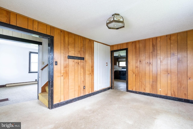 carpeted spare room featuring a baseboard radiator, wooden walls, stairway, and visible vents