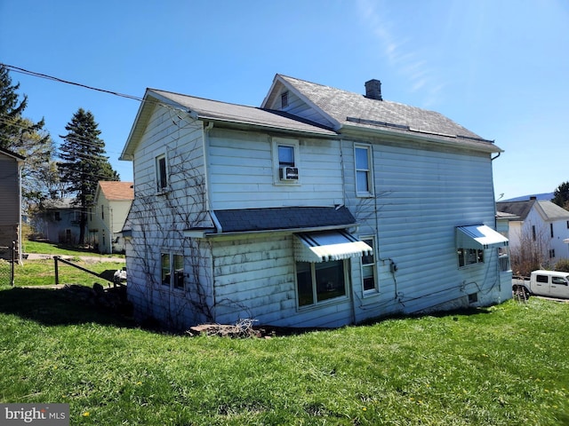 rear view of property featuring a chimney, a yard, and a shingled roof