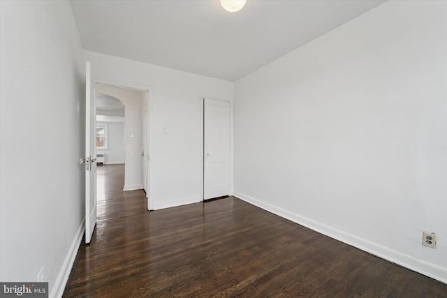 unfurnished bedroom featuring baseboards, dark wood-style floors, and arched walkways