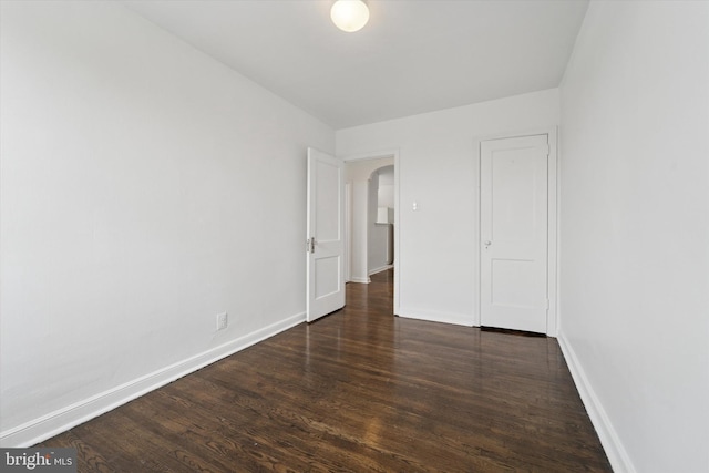 unfurnished bedroom featuring arched walkways, wood finished floors, and baseboards