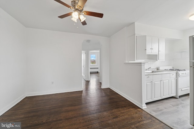 interior space with arched walkways, a sink, a ceiling fan, wood finished floors, and gas stove