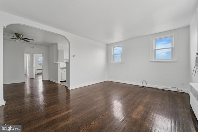 unfurnished living room featuring a ceiling fan, baseboards, arched walkways, and dark wood finished floors