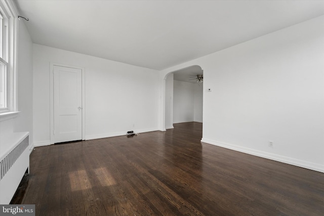 spare room with baseboards, wood finished floors, arched walkways, and radiator
