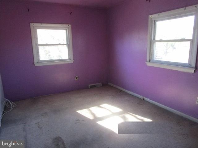 carpeted empty room featuring a wealth of natural light, visible vents, and baseboards