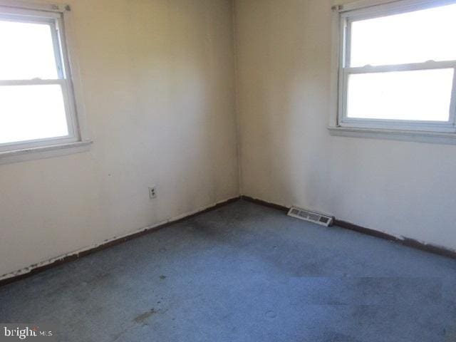 unfurnished room featuring dark carpet, a healthy amount of sunlight, and visible vents