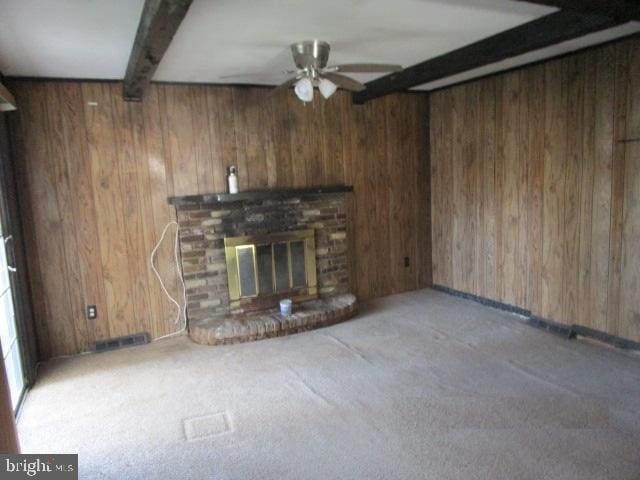 unfurnished living room with beam ceiling, visible vents, a ceiling fan, a brick fireplace, and wooden walls