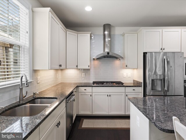 kitchen with a sink, backsplash, white cabinetry, wall chimney range hood, and appliances with stainless steel finishes