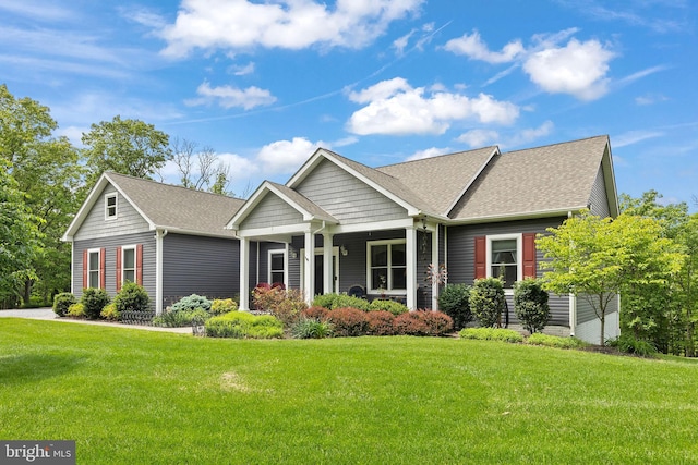 view of front facade with a front yard, a shingled roof, and covered porch