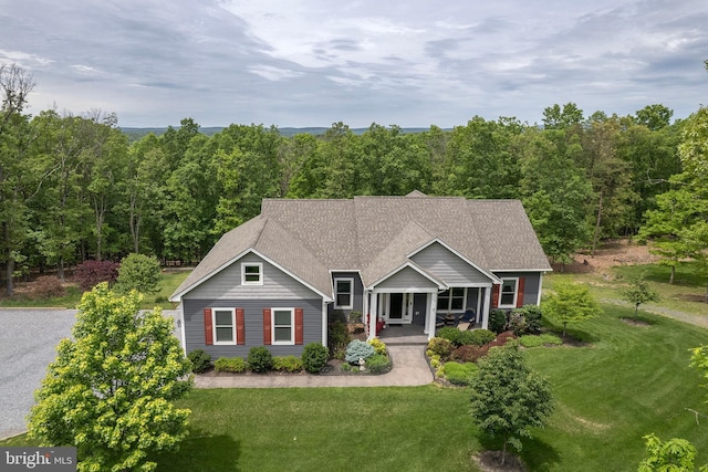 view of front facade featuring a front yard, a porch, a wooded view, and roof with shingles