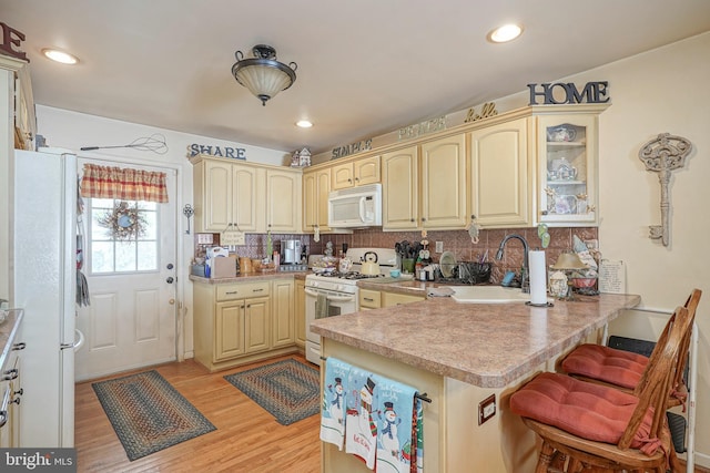 kitchen with a sink, tasteful backsplash, a breakfast bar area, a peninsula, and white appliances