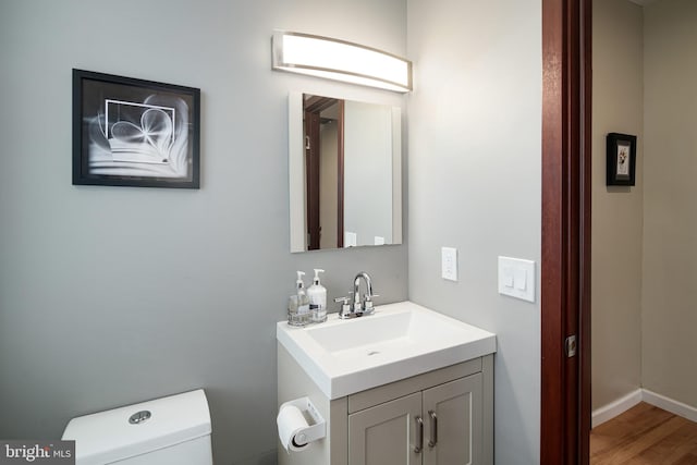 half bathroom with toilet, wood finished floors, and vanity