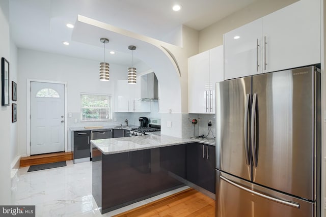 kitchen featuring white cabinets, stainless steel appliances, a peninsula, and wall chimney exhaust hood