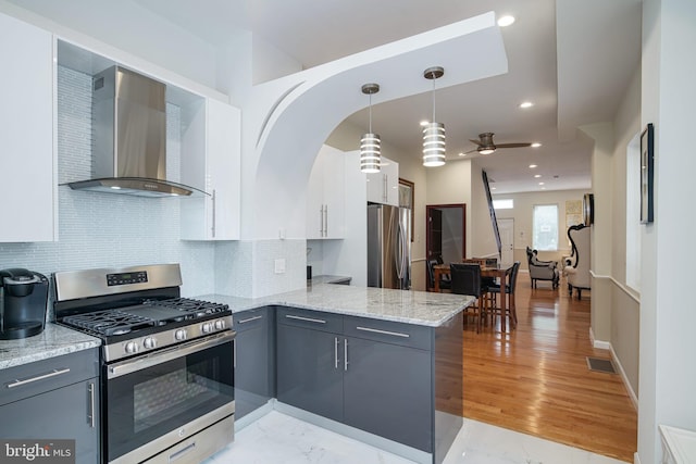 kitchen featuring wall chimney range hood, white cabinets, stainless steel appliances, a peninsula, and gray cabinetry