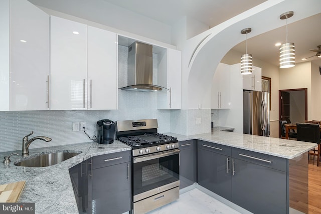 kitchen featuring wall chimney range hood, a sink, a peninsula, stainless steel appliances, and white cabinetry