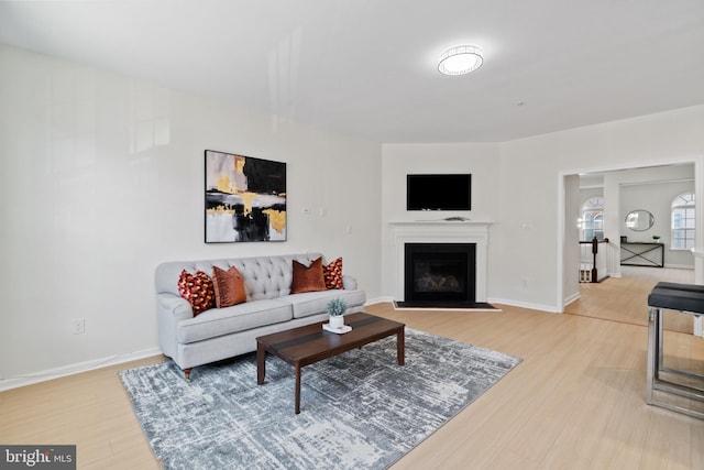 living area featuring baseboards, a glass covered fireplace, and light wood-style floors