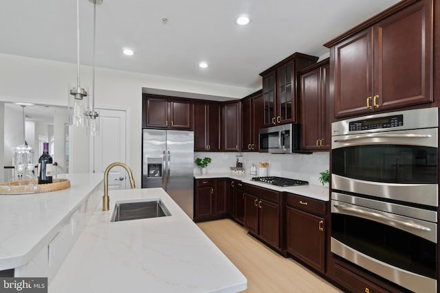 kitchen with stainless steel appliances, a sink, decorative light fixtures, light stone countertops, and light wood-style flooring