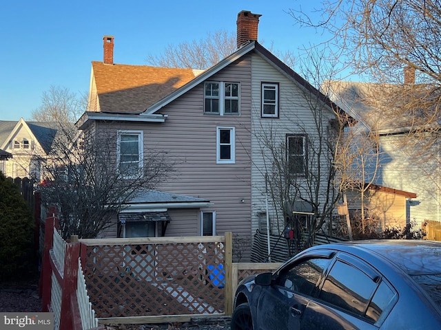 back of house featuring fence, roof with shingles, and a chimney