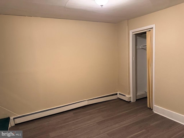 unfurnished bedroom with a baseboard heating unit, dark wood-style flooring, and baseboards