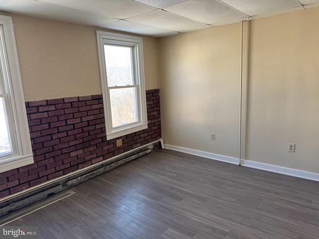 spare room with a baseboard radiator, brick wall, a paneled ceiling, and dark wood finished floors