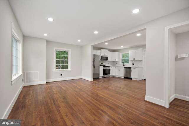 unfurnished living room featuring dark wood-style floors, visible vents, a healthy amount of sunlight, and baseboards