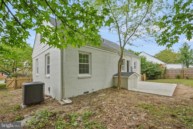 exterior space with cooling unit, a patio area, roof with shingles, fence, and brick siding