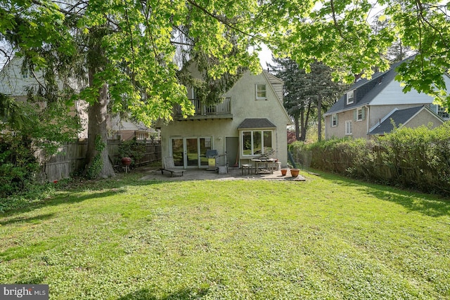 rear view of property featuring fence, stucco siding, a balcony, a lawn, and a patio
