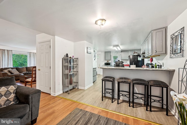 kitchen featuring freestanding refrigerator, open floor plan, a peninsula, gray cabinetry, and light wood-type flooring